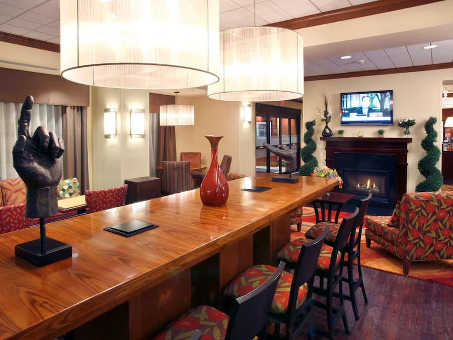 Un vestíbulo de hotel con un mostrador de recepción de madera, asientos cómodos, una chimenea y un televisor.