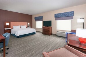 A hotel room with a bed, a desk, a chair, a TV, and a lamp.