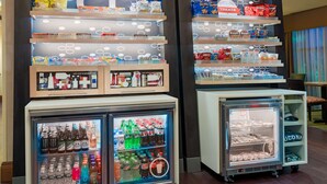 A snack display with various chips and snacks, a refrigerated display with beverages, and a cooler with bottled water. - Hampton Inn Springfield South Enfield (Enfield)