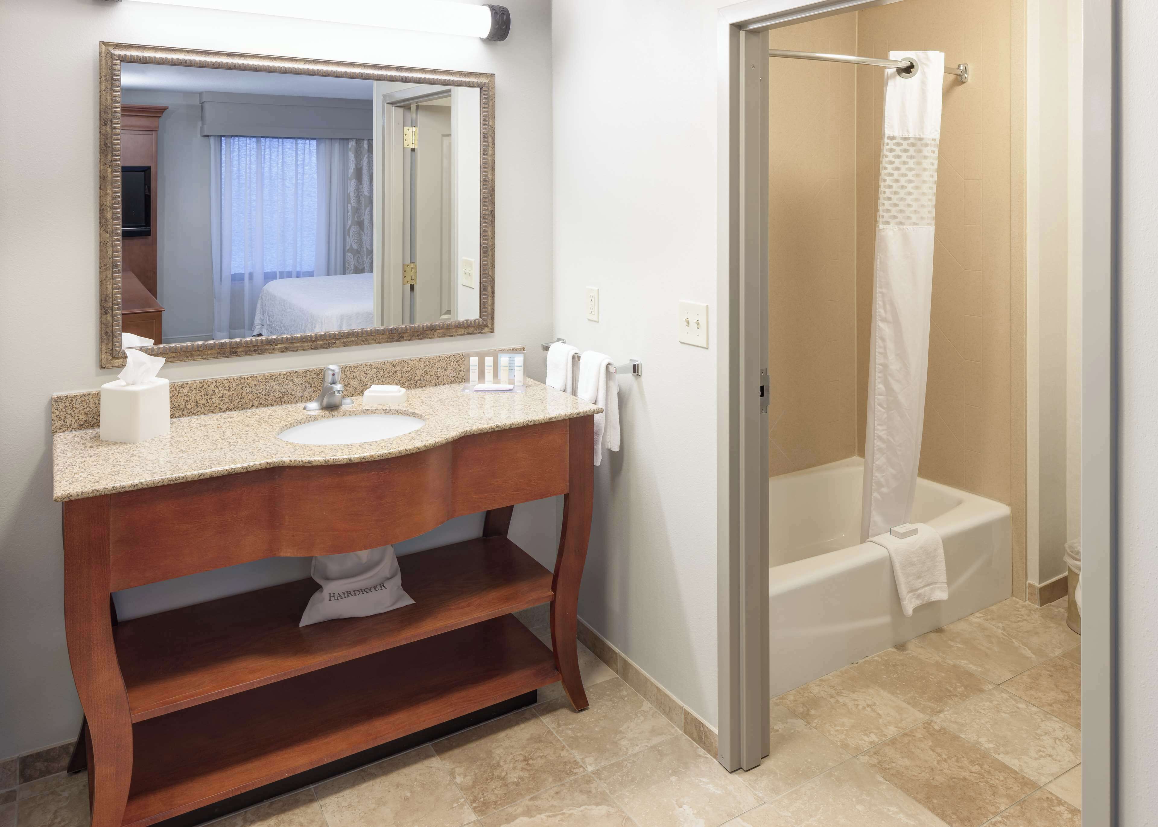 A bathroom with a granite countertop sink, a mirror, a hairdryer, and a shower with a glass door.