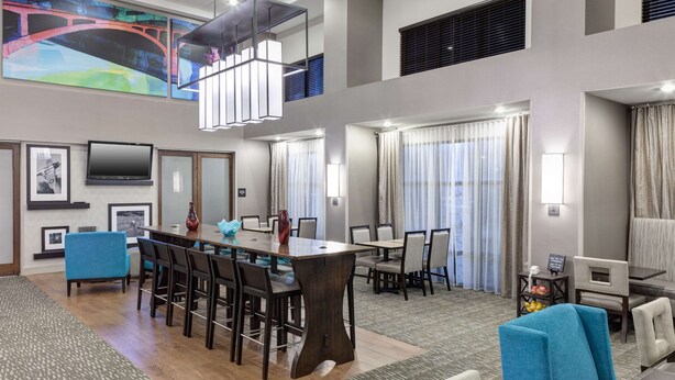 A hotel lobby with a central dining area, multiple seating options, and a large TV screen on the wall. - Hampton Inn & Suites Cedar Rapids - North (Cedar Rapids)