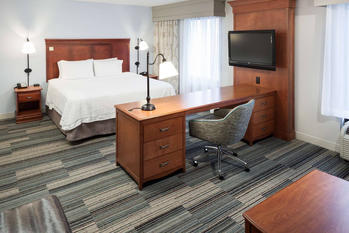 A hotel room with a bed, desk, chair, TV, and bedside lamps.