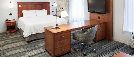 A hotel room with a bed, desk, chair, TV, and bedside lamps.