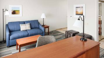 A modern hotel room with a blue sofa, a wooden desk, two lamps, and two framed pictures on the walls.