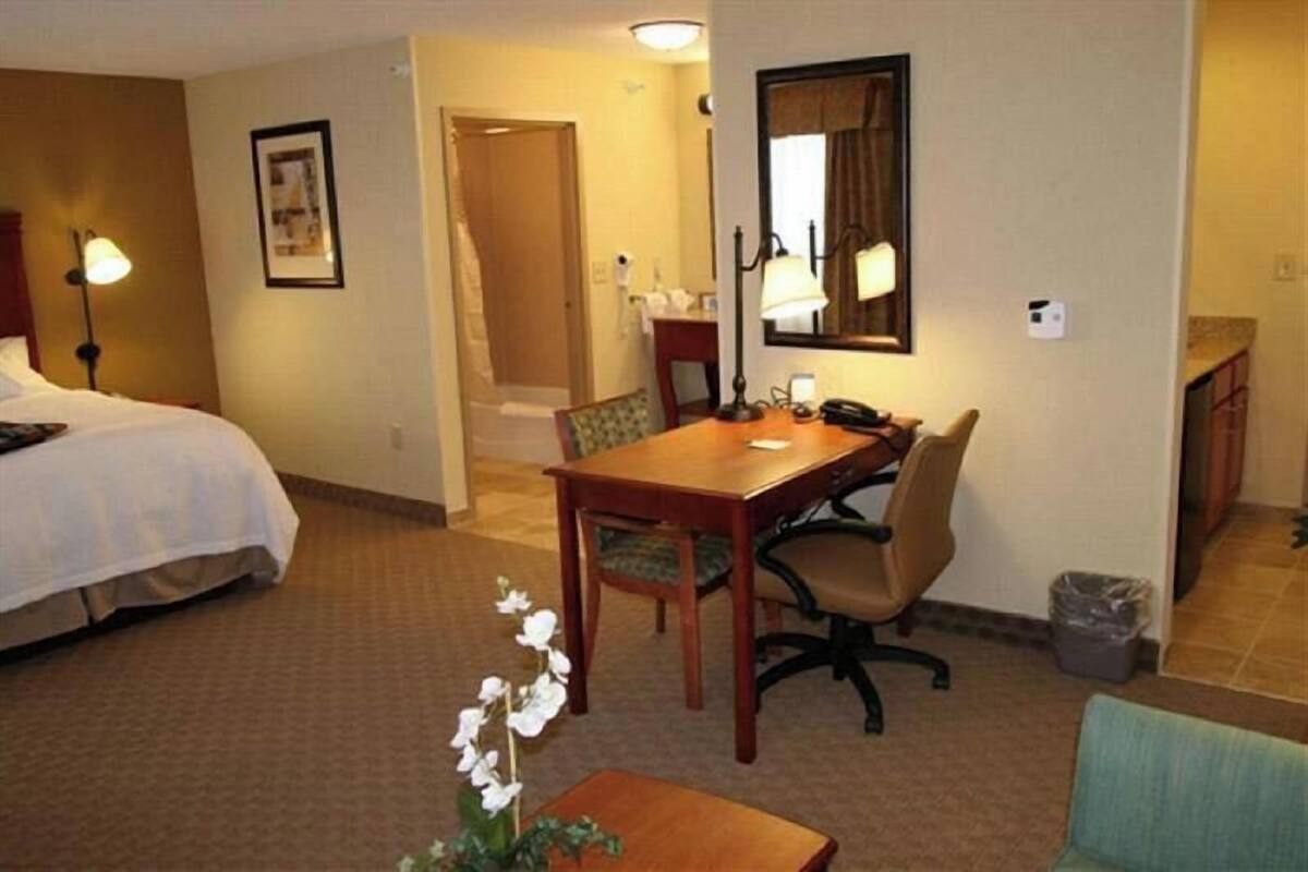A hotel room with a bed, a desk, a chair, a lamp, and a trash bin.