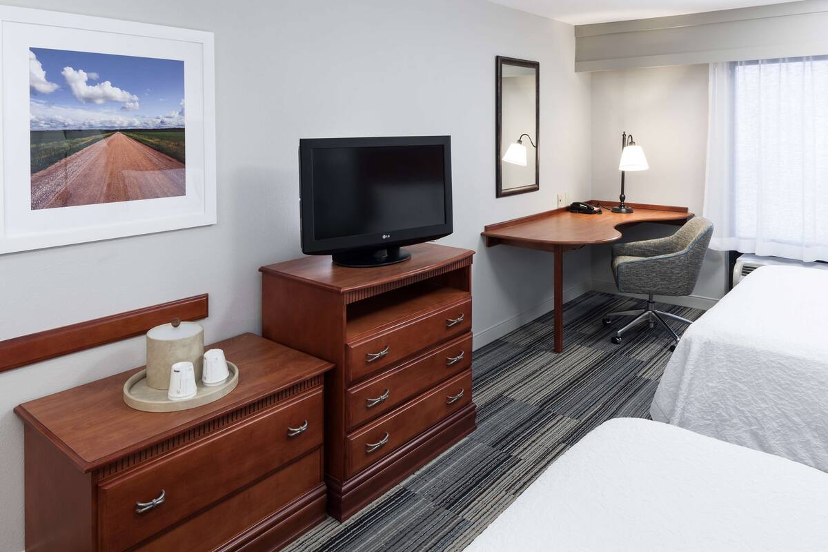 A hotel room with a bed, a desk with a chair, a television, a dresser, and a framed picture on the wall.