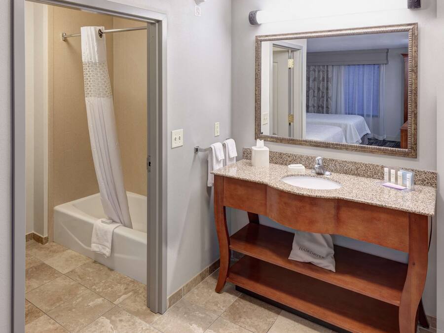 A bathroom with a shower, a sink, a mirror, and a hairdryer on a shelf.