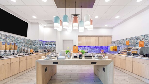 Un espace cuisine moderne doté d’un îlot central, de plusieurs plans de travail et d’un crédence recouverte de carreaux bleus.