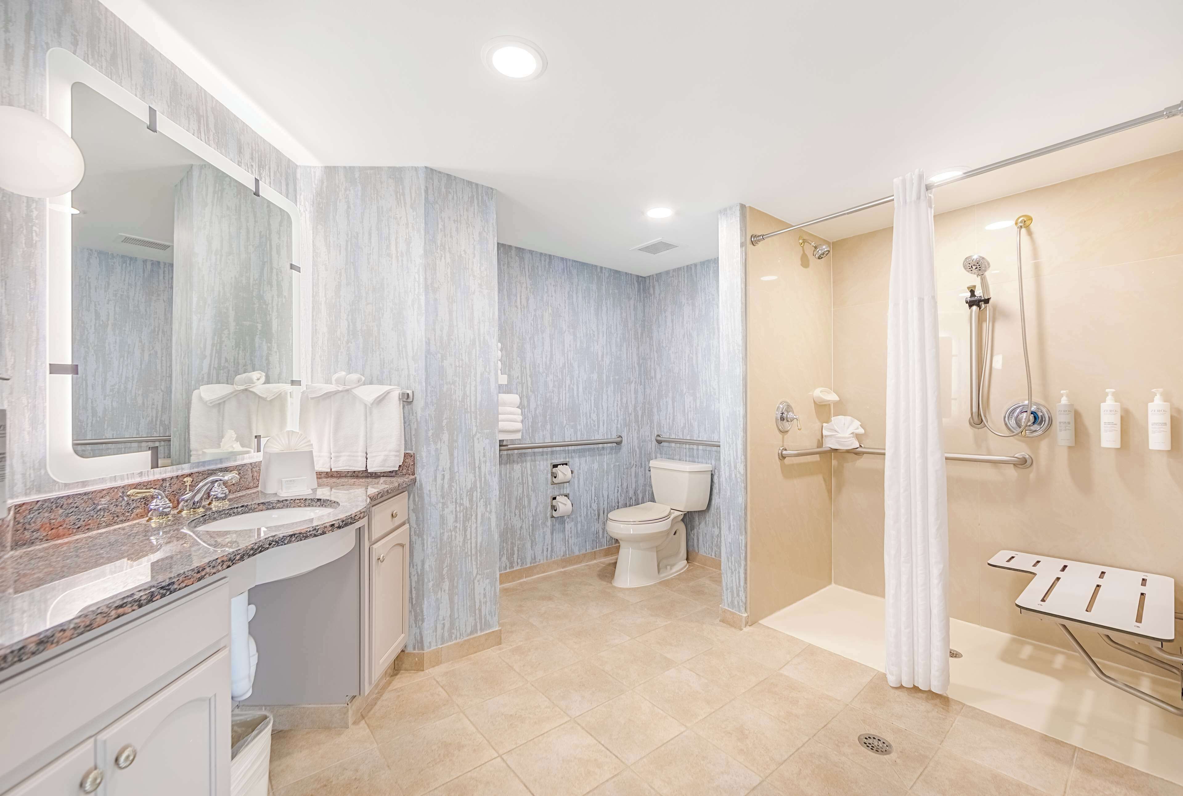 A modern bathroom with a granite countertop sink, a toilet, and a walk-in shower with a glass door.