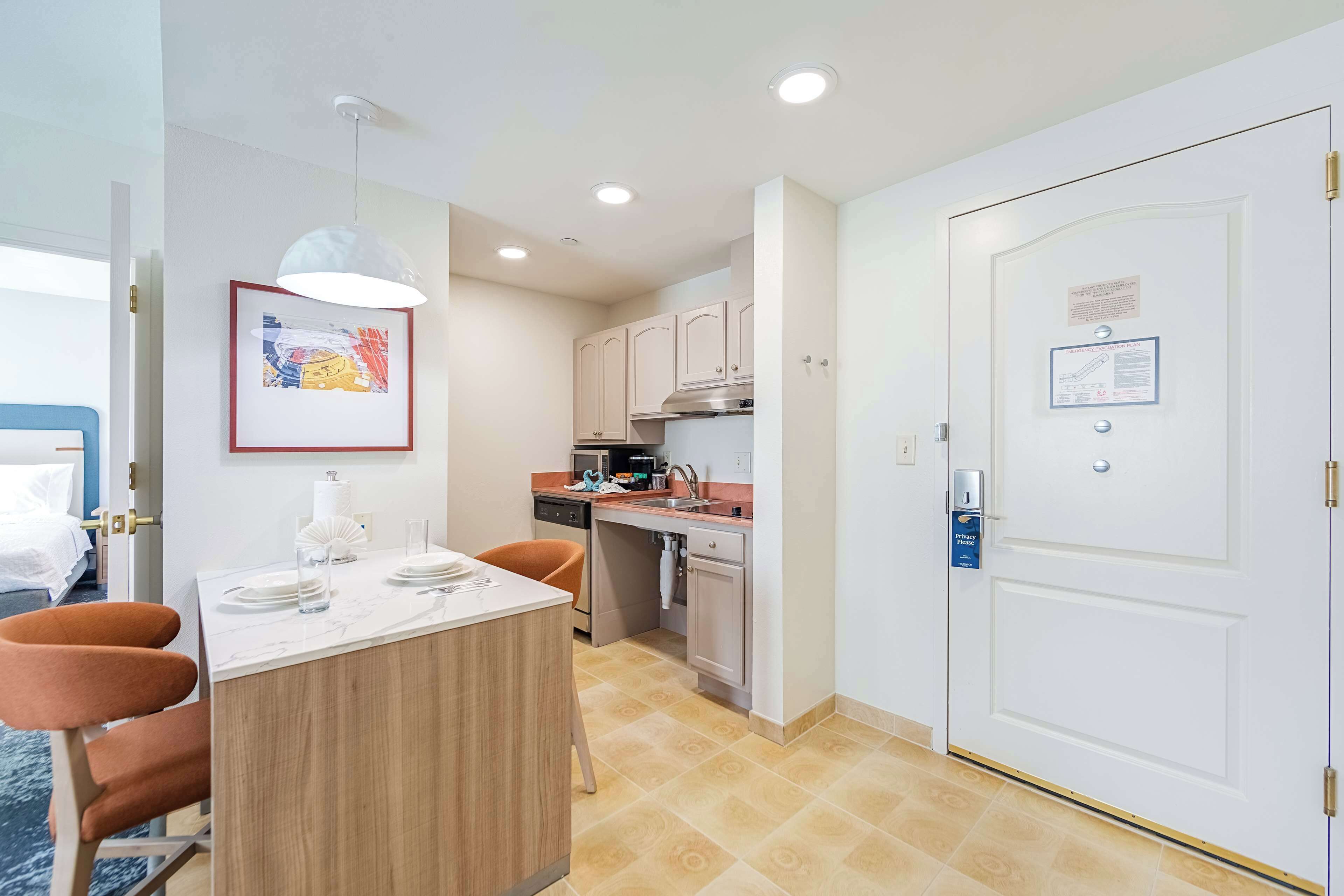 A compact hotel room with a dining area, kitchenette, and a door with a privacy card.