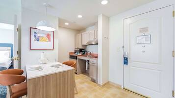 A compact hotel room with a dining area, kitchenette, and a door with a privacy card.