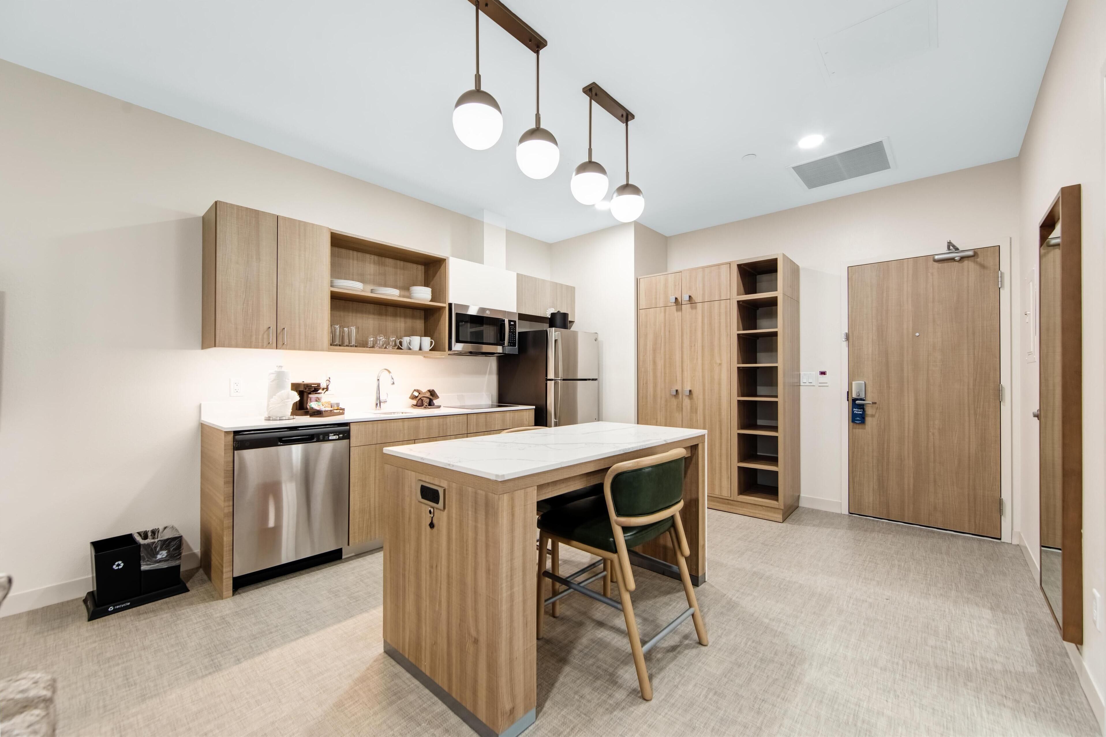 A modern kitchen with wooden cabinets, a built-in microwave, and a central island with a chair.