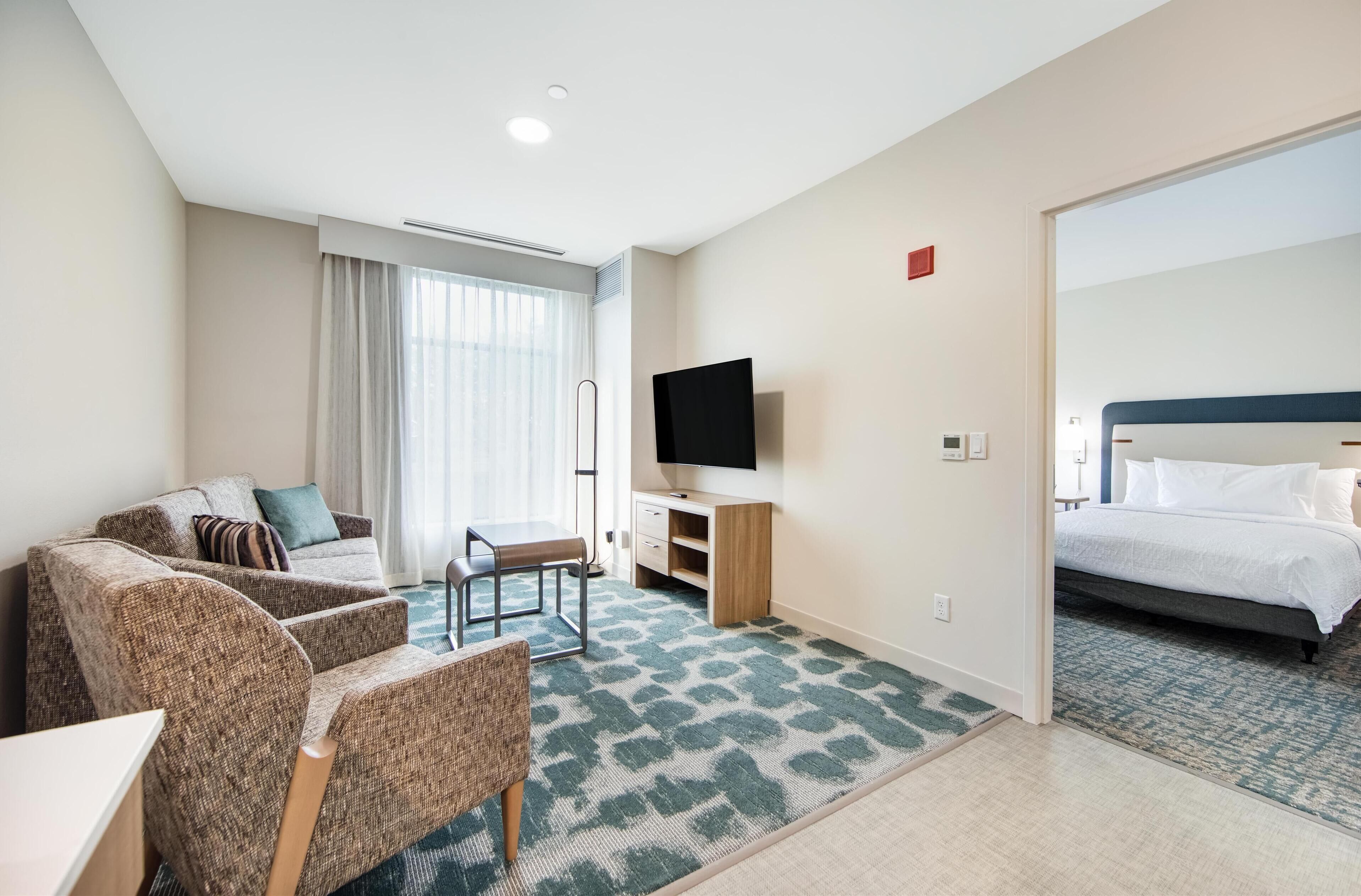 Hotellihuone, jossa on sohva, tuoli, televisio, sänky ja työpöytä.