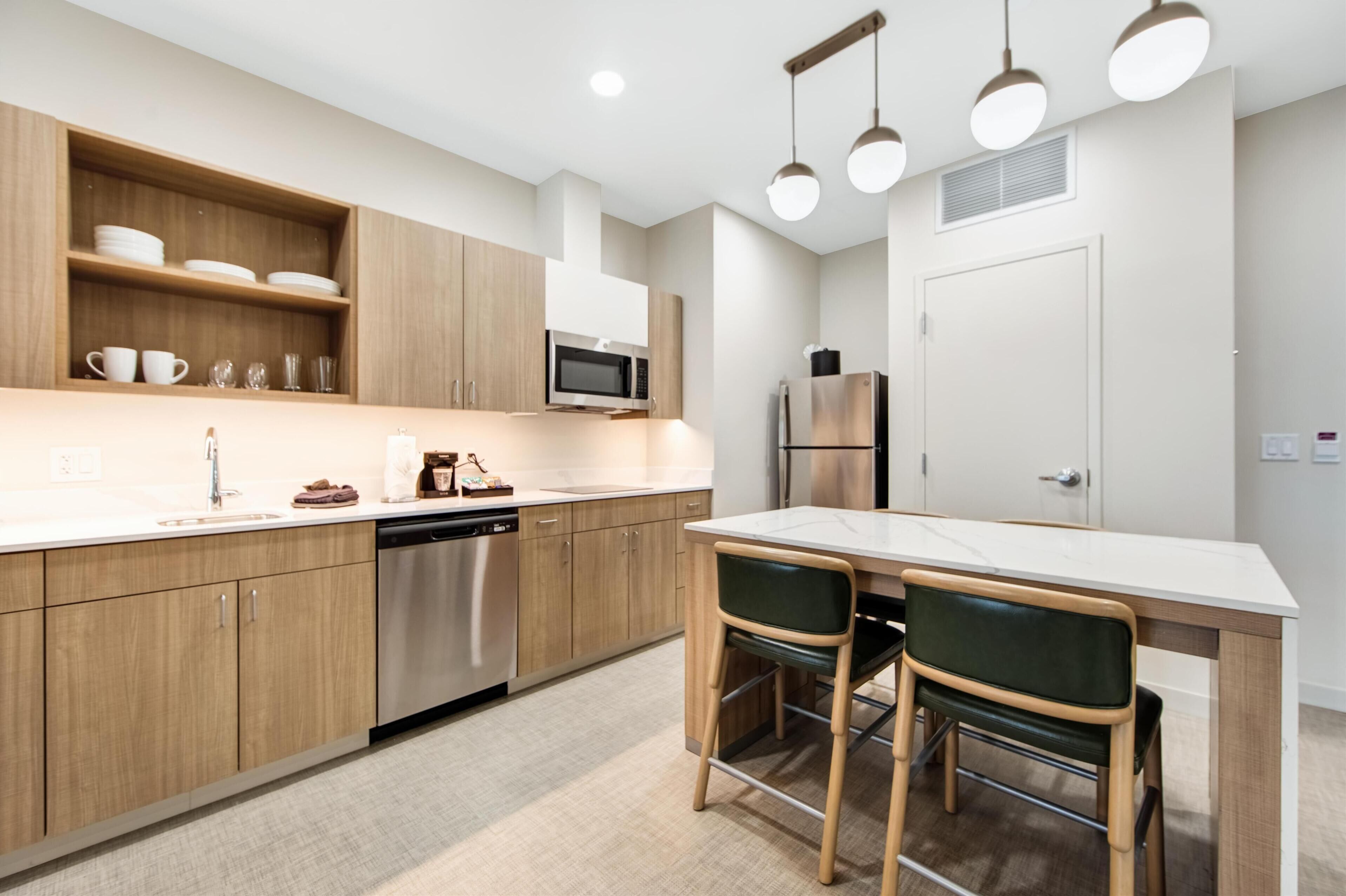 A modern kitchen with wooden cabinets, a microwave, a dishwasher, and a refrigerator. There is a dining table with two chairs.