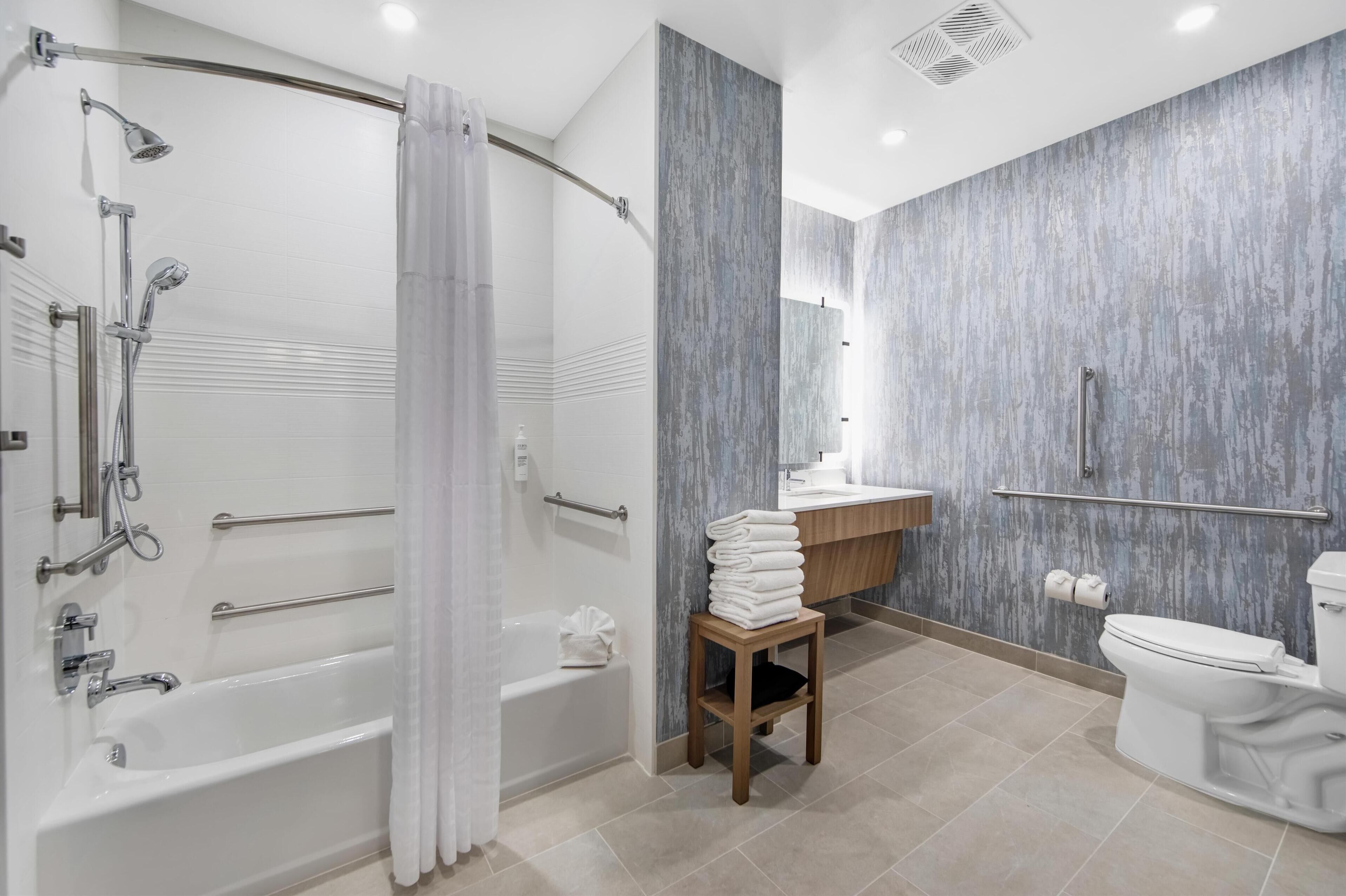 Un baño moderno con cabina de ducha, barras de apoyo, bañera, inodoro y tocador con espejo.
