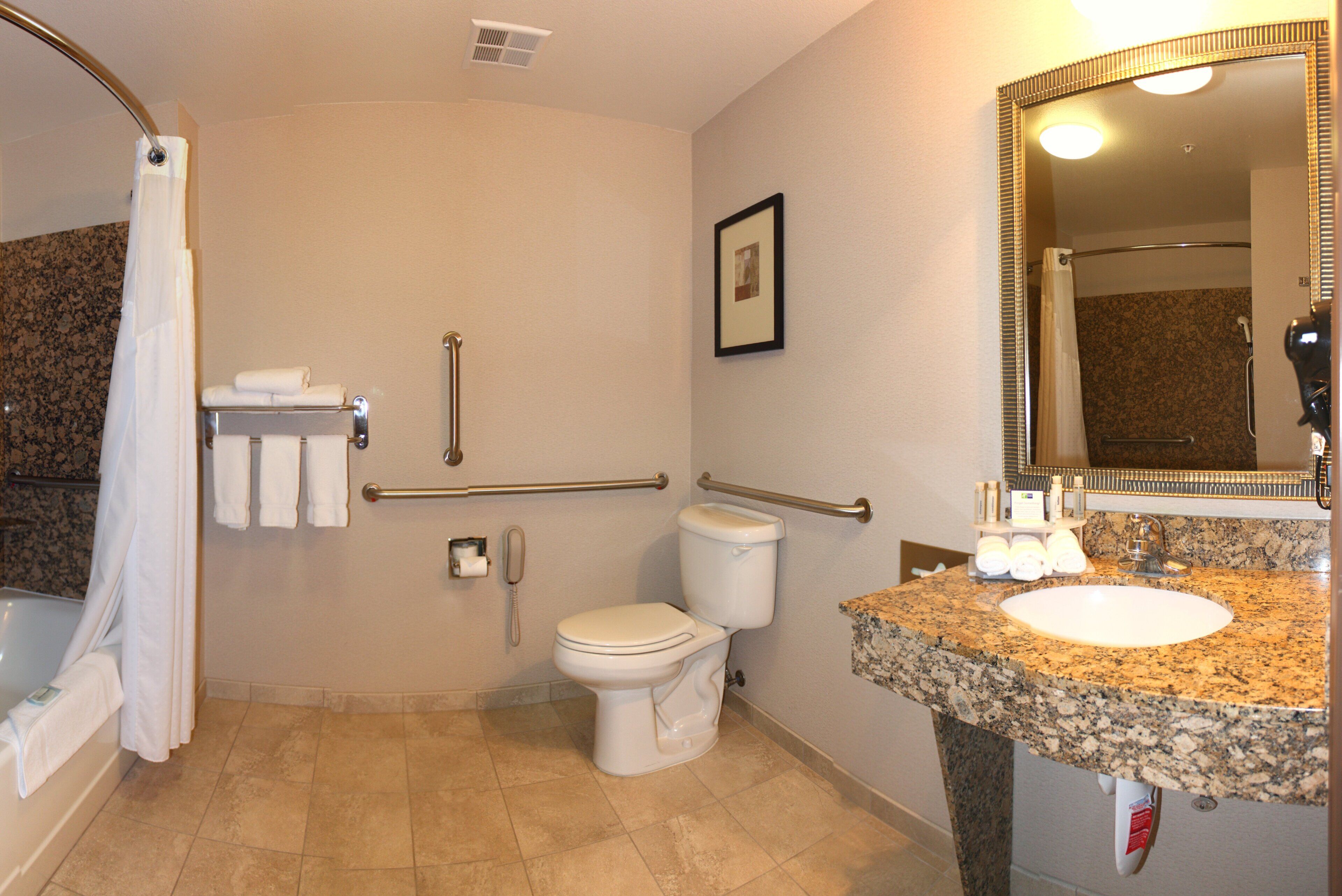 A bathroom with a toilet, sink, shower, and grab bars.