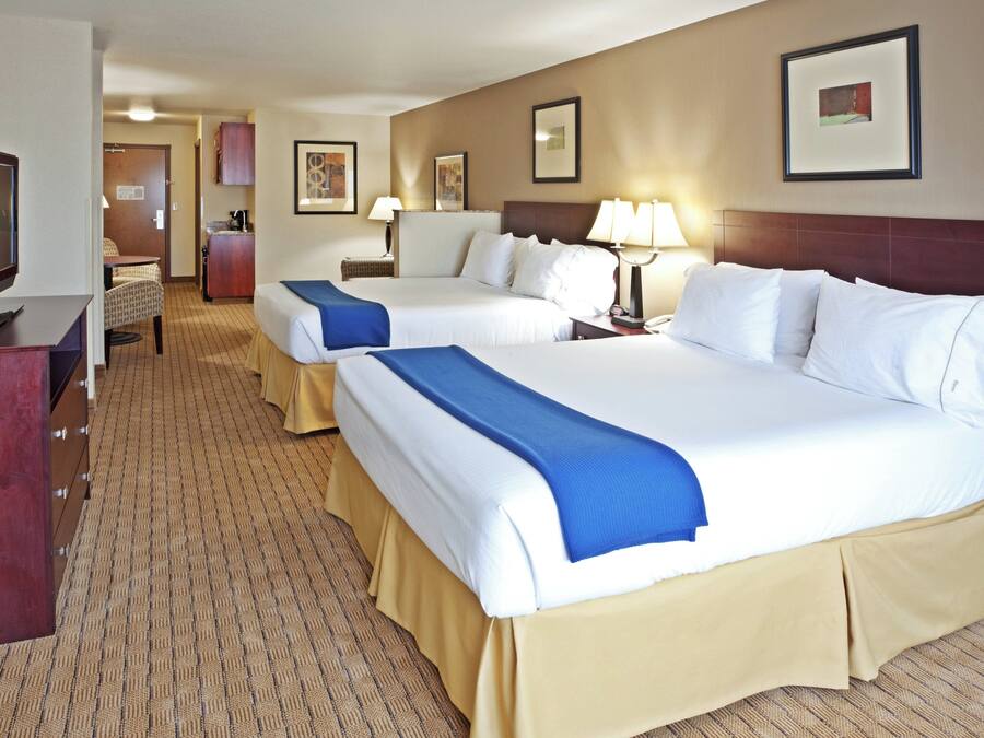 Quarto de hotel com duas camas, uma escrivaninha, televisão e cozinha compacta.