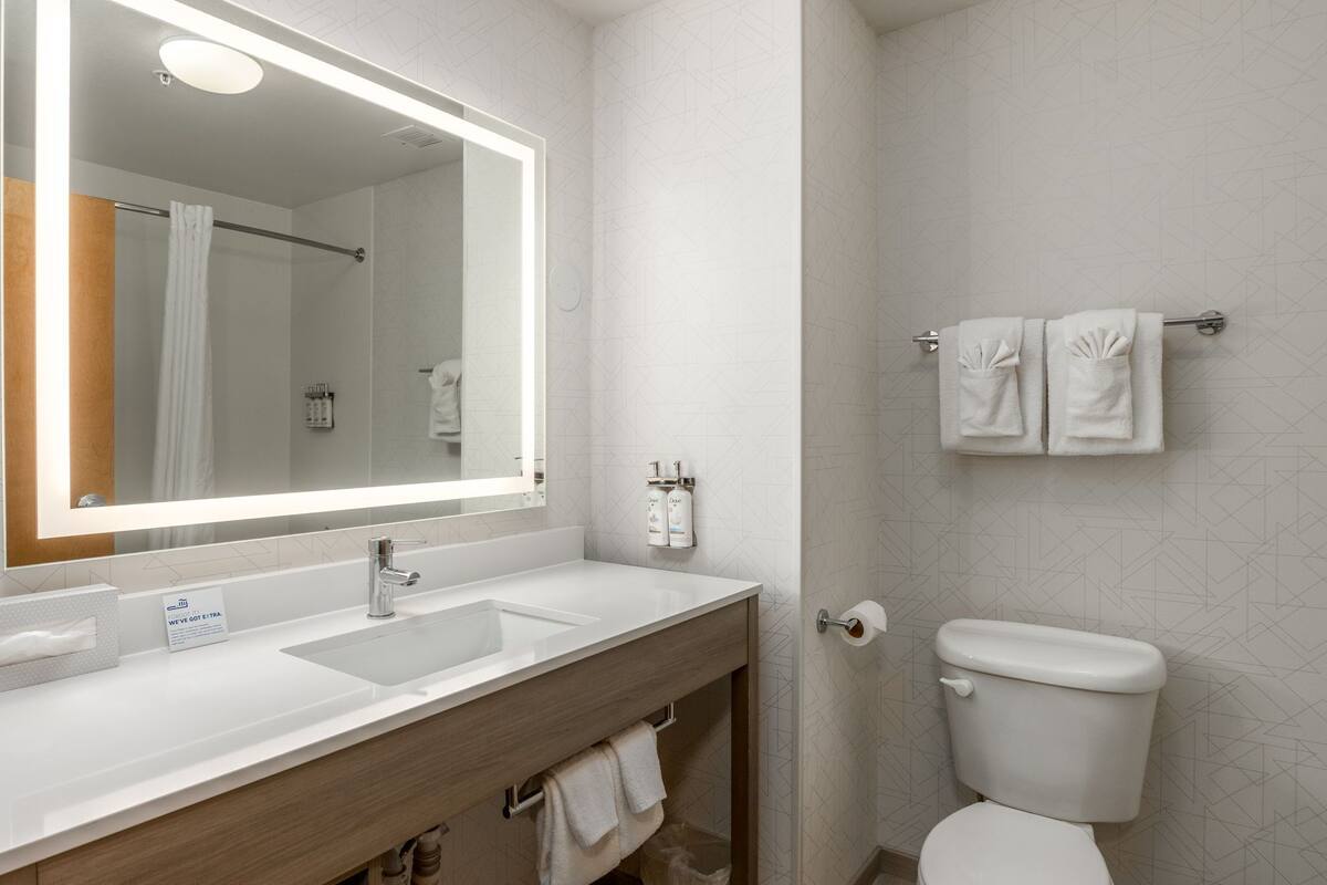 A modern bathroom with a large mirror, two sinks, a toilet, and a towel rack.