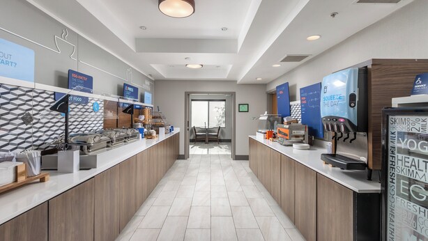 A modern hotel lobby with a long reception desk, a coffee machine, and a digital screen displaying information. - Holiday Inn Express Hotel & Suites Vancouver Mall by IHG (Vancouver)