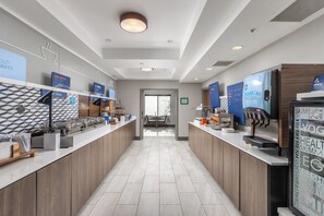 A modern hotel lobby with a long reception desk, a coffee machine, and a digital screen displaying information. - Holiday Inn Express Hotel & Suites Vancouver Mall by IHG (Vancouver)
