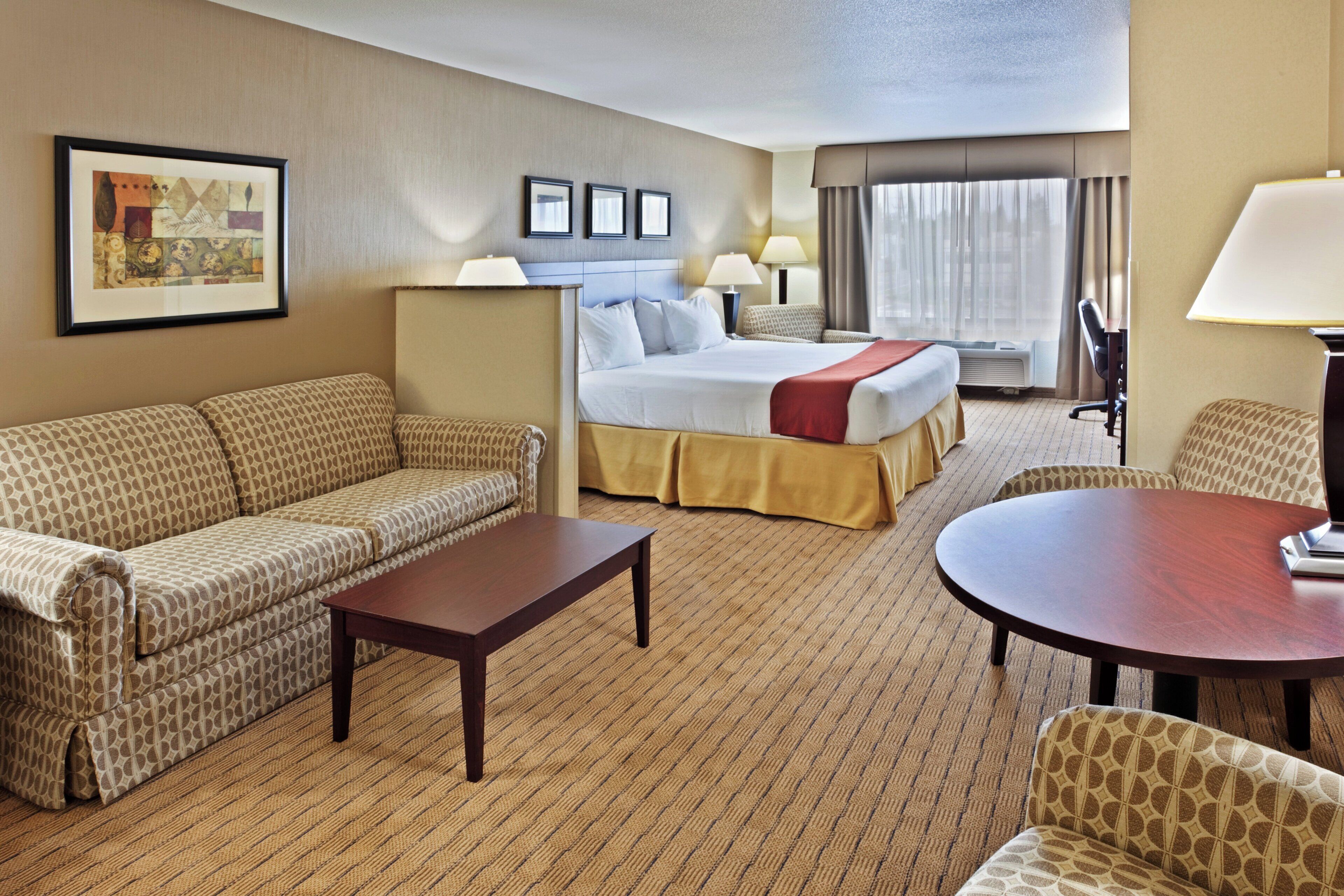 A hotel room with a bed, a sofa, a coffee table, a desk, and a chair.