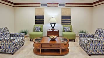 A room with a central coffee table, two green sofas with patterned cushions, and a lamp on a side table.