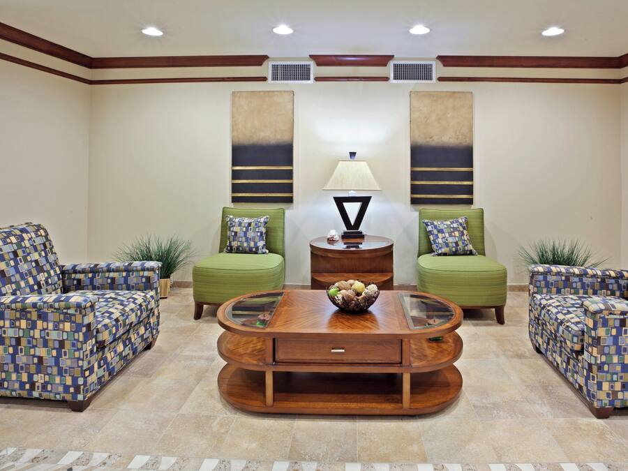 A room with a central coffee table, two green sofas with patterned cushions, and a lamp on a side table.