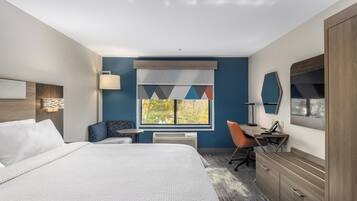A hotel room with a large bed, a desk, a chair, a wardrobe, and a window with a view of trees.
