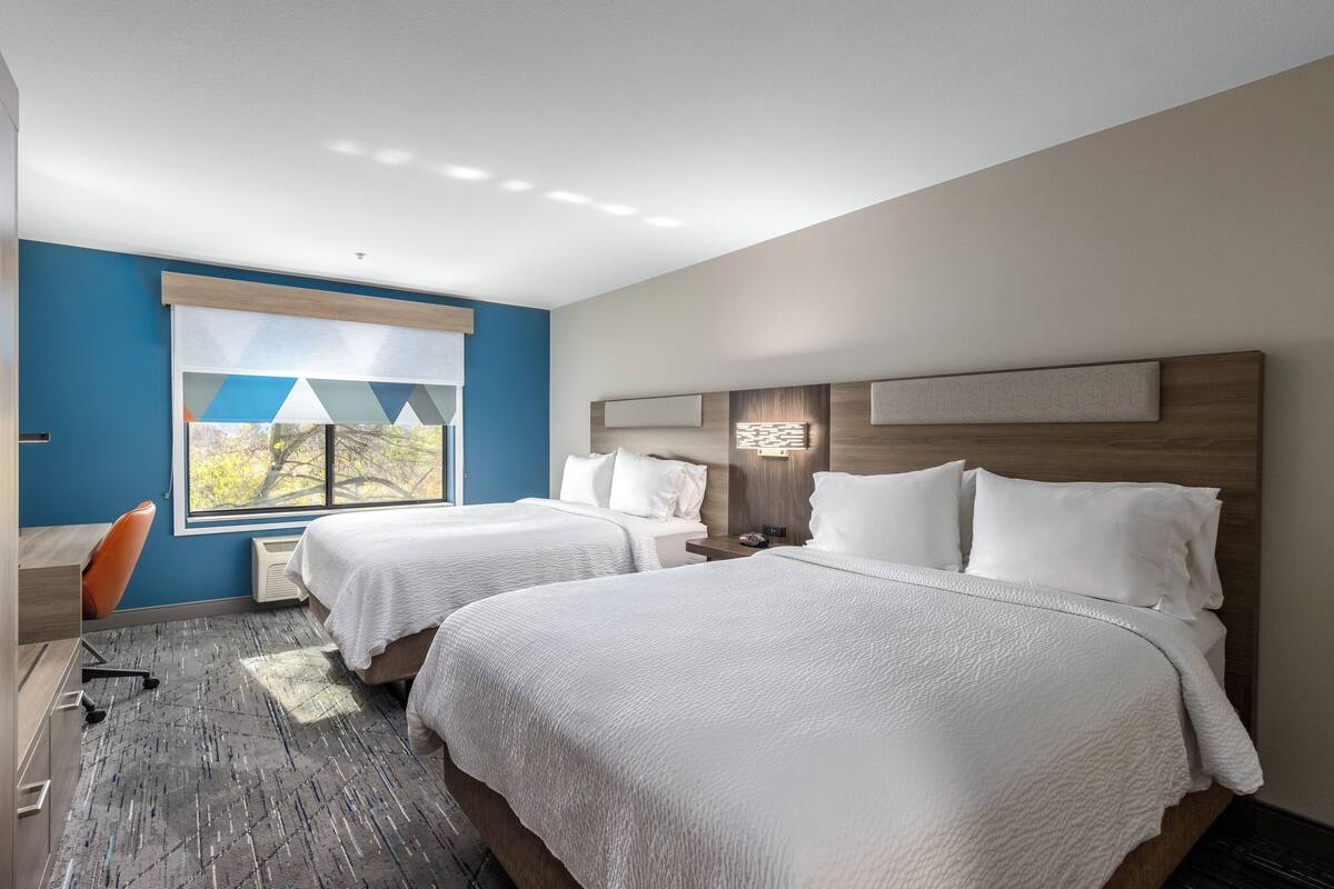 A modern hotel room with two beds, a desk, and a chair.
