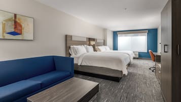 A hotel room with a blue sofa, two beds, a desk, and a large window.