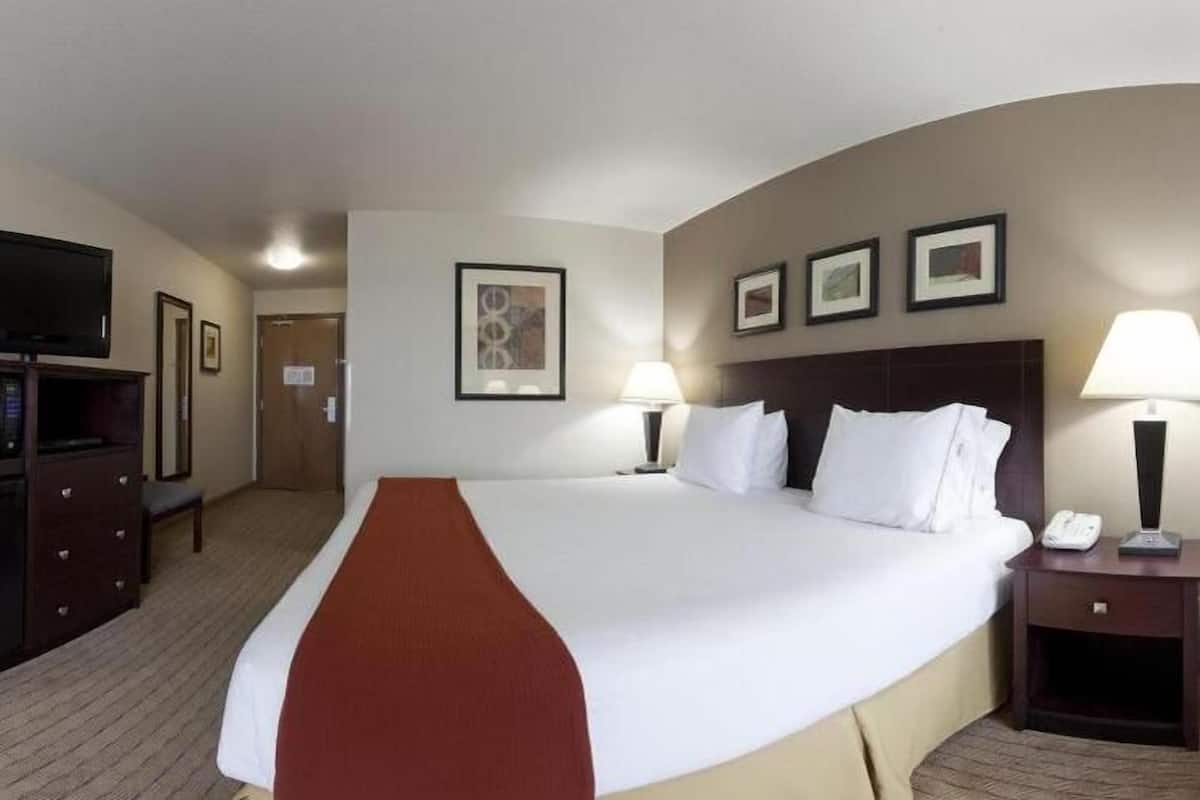 A hotel room with a large bed, two bedside lamps, a TV, a desk, and a mirror.