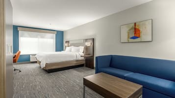 A modern hotel room with a bed, a blue sofa, a wooden coffee table, and a painting on the wall.
