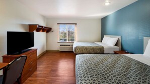 Ein Hotelzimmer mit Flachbildfernseher, zwei Betten mit gemusterten Bettwäsche, einer Holzkommode, einem Schreibtisch und einem Fenster mit Jalousien.