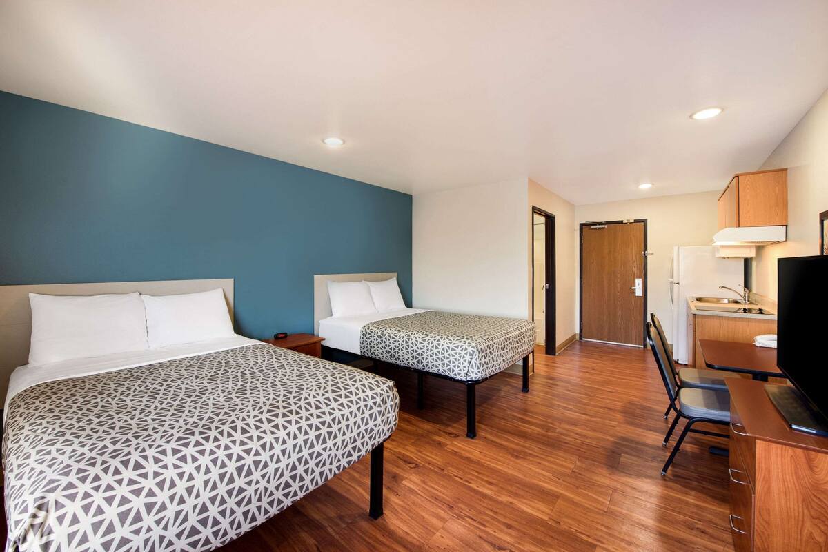 Une chambre d’hôtel avec deux lits, un plancher en bois, une télévision et une kitchenette.