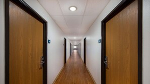 Ein langer, schmaler Gang mit Holztüren an beiden Seiten und einer gefliesten Decke.