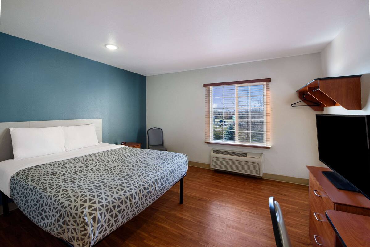 Une chambre à coucher avec un lit, une télévision, une fenêtre avec des stores et un radiateur.