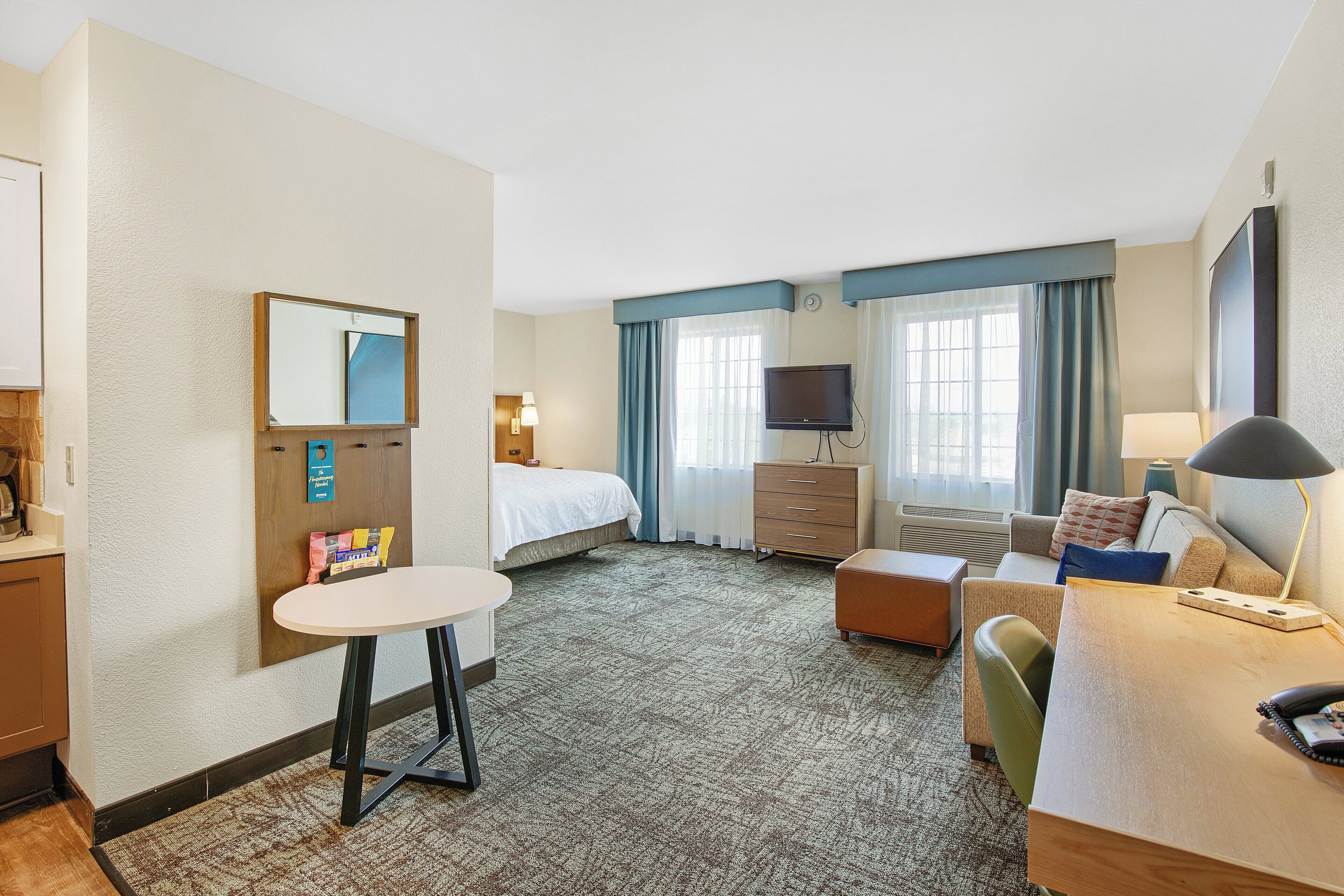 Ein Hotelzimmer mit Bett, Schreibtisch, Stuhl, Fernseher, Lampe und einem kleinen Tisch.