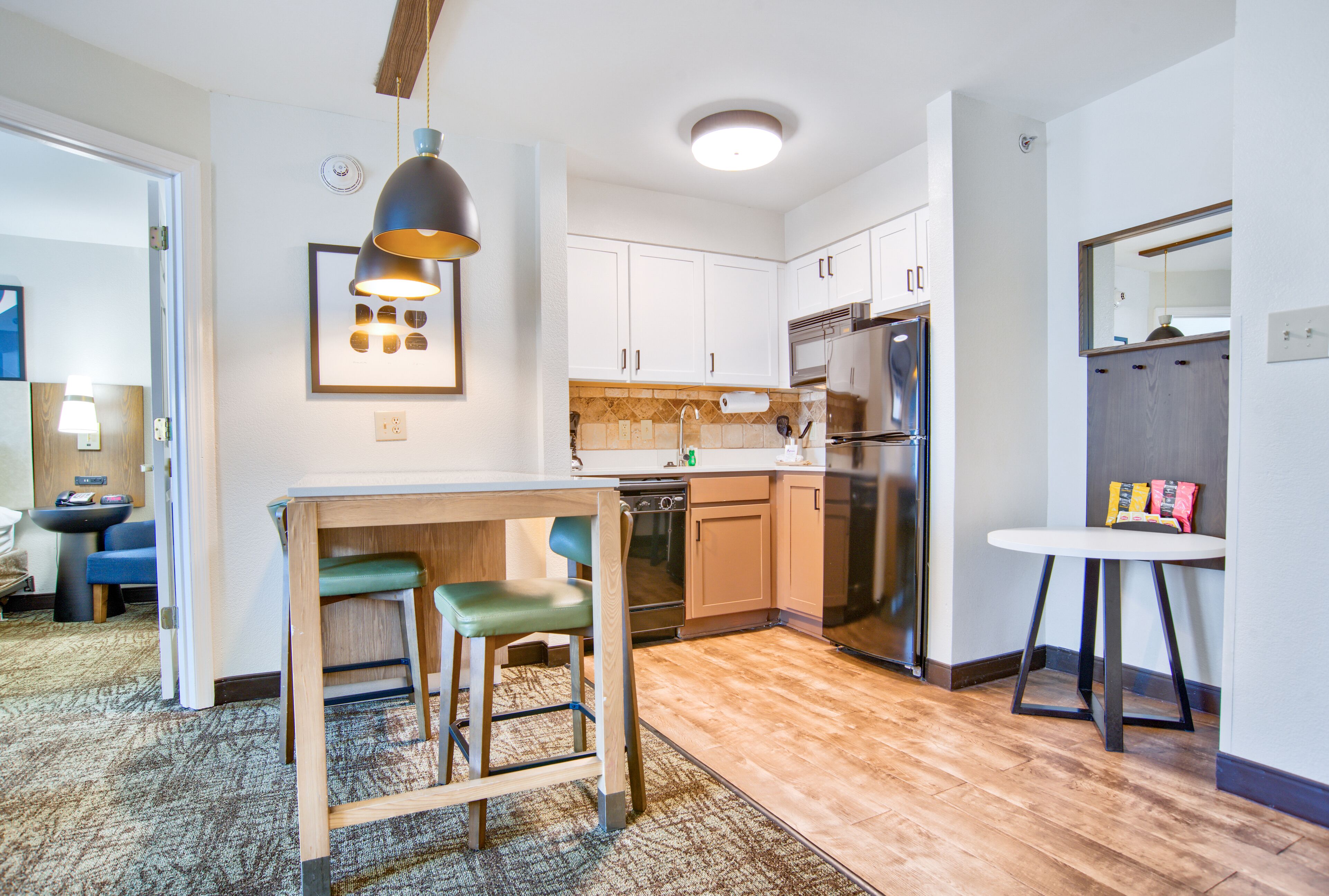 A modern kitchen with white cabinets, a built-in oven, a stainless steel refrigerator, and a small dining area with a table and chairs.