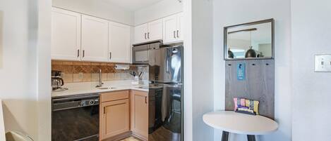 A compact kitchen with white cabinets, stainless steel appliances, and a small table with a mirror.