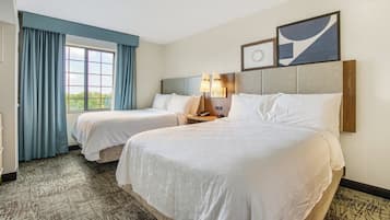 Una habitación de hotel con dos camas, un ventanal con cortinas, un cabecero con lámparas fijadas a la pared y una obra de arte abstracta enmarcada sobre las camas.