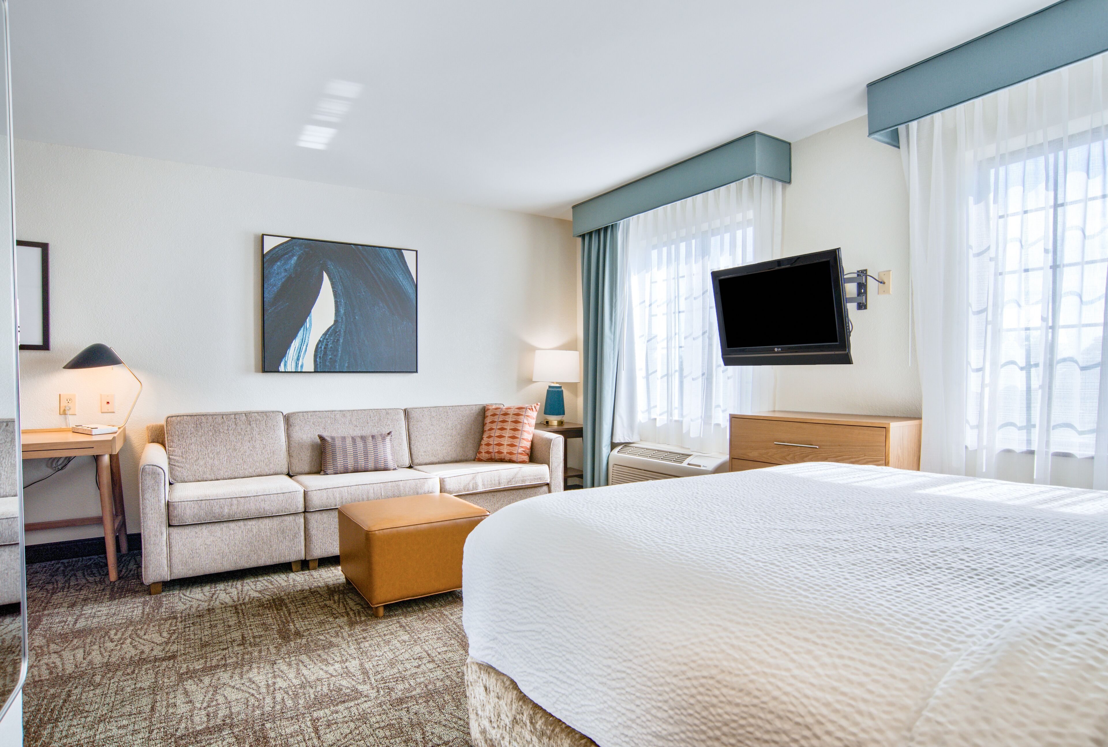 Une chambre d’hôtel avec un lit, un canapé, un bureau, une télévision et un tableau au mur.