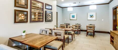 A dining area with wooden tables and chairs, framed artwork on the walls, and a wooden cabinet.