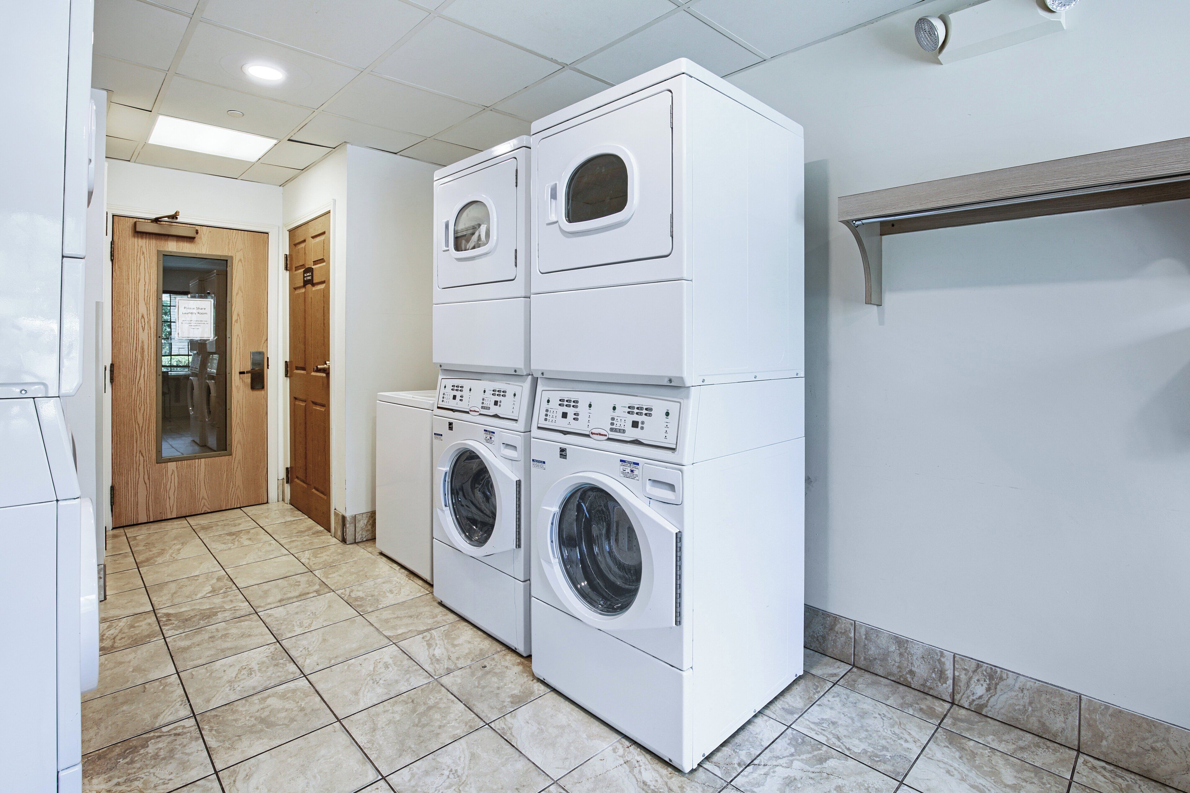 A laundry room with stacked washing machines and dryers, a wooden door, and tiled flooring.