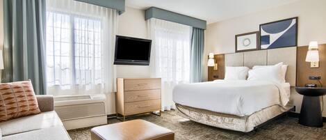Quarto de hotel com cama, cômoda, televisão e sofá.
