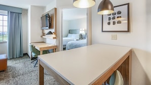 Habitación de hotel con escritorio, cama, televisor y un cuadro en la pared.