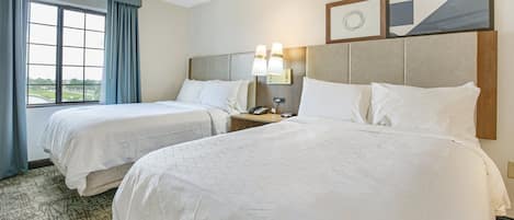 Habitación de hotel con dos camas, un ventanal con cortinas, una mesita de noche con teléfono y decoración en la pared.