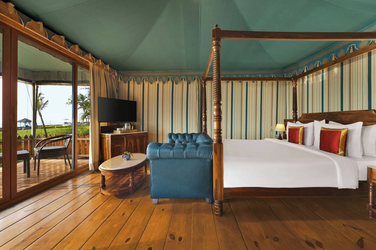 Un dormitorio espacioso con cama con dosel, televisión, zona de estar con una mesa redonda y vistas al exterior.