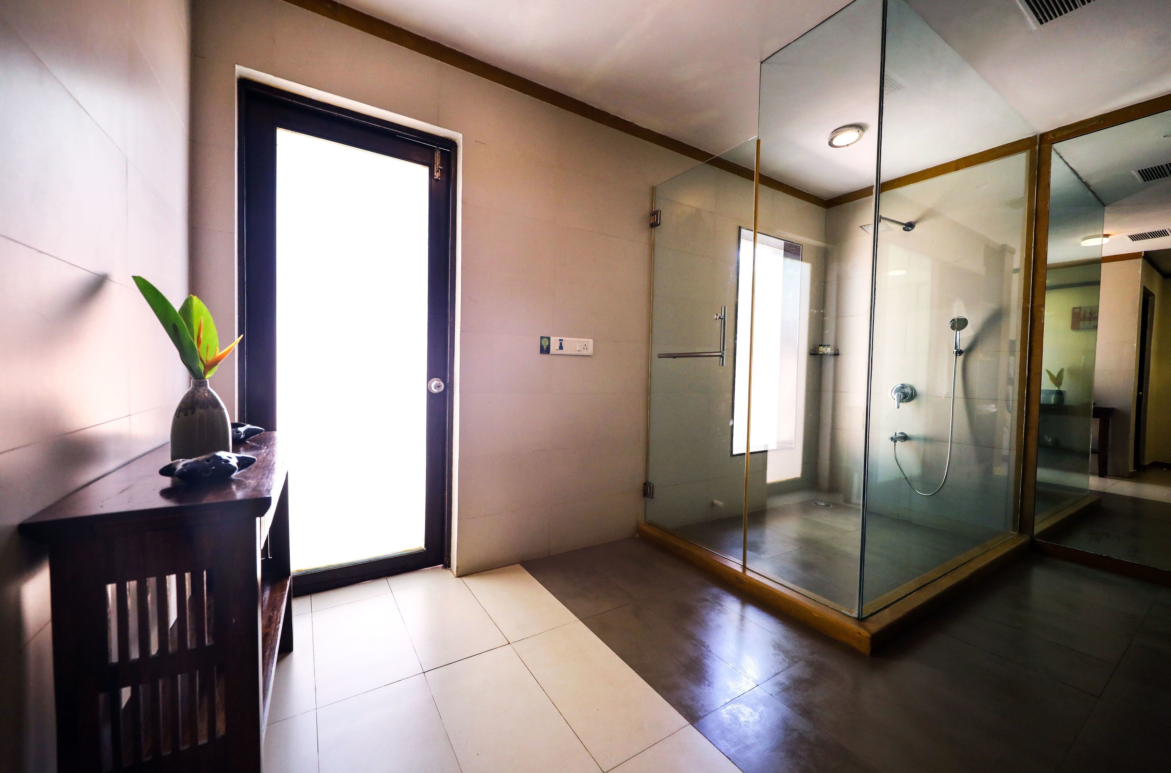 A modern bathroom with a glass-enclosed shower, a wooden vanity with a vase of flowers, and a large mirror.