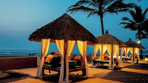 A beach with thatched-roof cabanas, each with a canopy and a single green lounge chair.