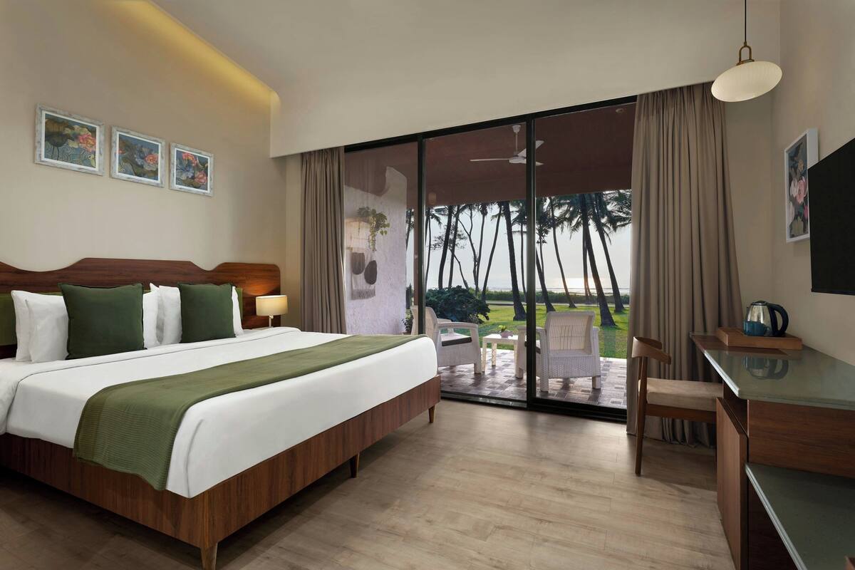 Habitación de hotel con una cama grande, un escritorio y vistas a palmeras a través del ventanal corredera.